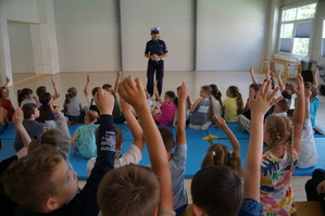 policjantka stoi przodem przed nią SIEDZĄ DZIECI I CZĘŚC Z NICH ZGŁASZA SIĘ