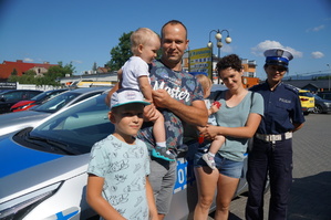 rodzina ojciec matka i troje dzieci i policjantka stoją obok siebie na tle radiowozu zdjęcie zrobione w centrum miasta