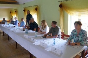 zdjęcie zrobione w sali za stołem siedzą zaproszeni gości prowadzący przedstawia gości