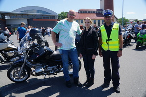 obok siebie stoją policjant kobieta i męzczyzna obok nich motocykl w tle inni motocykliści i motory