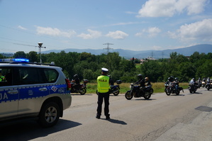 fragment radiowozu na środku zdjęcia stoi na ulicy policjant po drodze jadą motocykliści