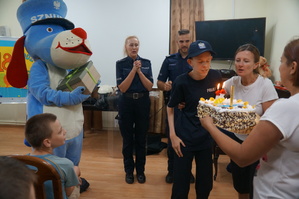 krzysiu zdmuchuje świeczkę z torta w tle policjanci sznupek i opiekunowie