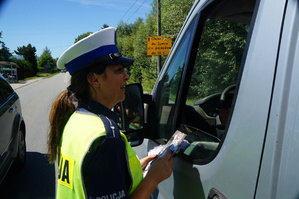 fragment samochodu i policjantki wręczajacej ulotki