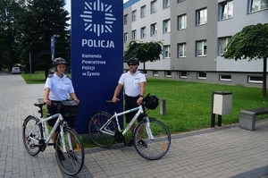 policjant i policjantka stoją obok pylonu komendy powiatowej policji w Żywcu z rowerami