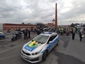 na pierwszym planie zaparkowany samochód na którym leżą odblaskowe kamizelki i opaski w tle zaparkowane motocykle