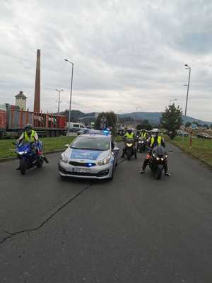 stoi policyjny radiowóz obok niego i za nim motocykliści na motorach