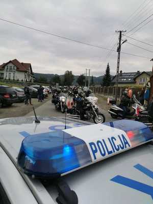 na pierwszym planie fragment radiowozu w tle motocykliści