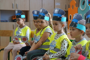 dzieci siedzą koło siebie na krzesłach mają założone odblaskowe kamizelki i zrobione policyjne czapki