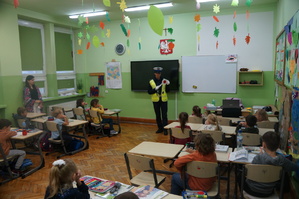 sala lekcyjna uczniowie siedzą tyłem w ławkach przed nimi stoi policjantka