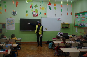 sala lekcyjna przed dziećmi stoi policjantka i prowadzi prelekcje uczniowie siedzą w ławkach