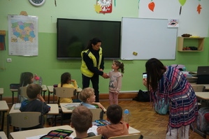 policjantka razem z jedną z uczennic wykonuje cwiczenie praktyczne reszta uczniów siedzi w ławce