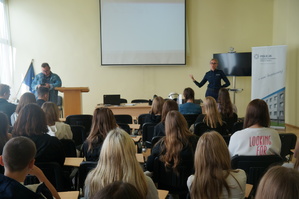 uczniowie na sali siedzą tyłem przed nimi stoi policjantka i prowadzi prelekcje obok stoi nauczyciel