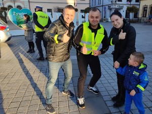 w centrum zdjęcia mężczyzna kobieta i dziecko obok stoi redaktor w tle rynek miasta