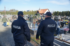 policjanci w czasie służby na cmentarzu w tle nagrobki i ludzie