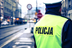 na zdjęciu policjant stoi tyłem w tle ulica