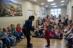 zdjęcie kolorowe  zrobione w sali widać na nim policjantkę która prowadzi prelekcję obok niej stoi uczennica reszta dzieci siedzi