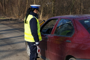 zdjęcie kolorowe zrobione na zewnątrz przedstawia policjantkę podczas kontroli stanu trzeźwości kierowcy samochodu