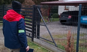 na zdjęciu kolorowym tyłem stoi policjant w tle budynek