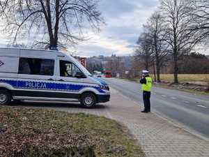 zdjęcie zrobione na zewnątrz widać ulice i policjanta który dokonuje pomiaru prędkosci obok zaparkowany radiowóz