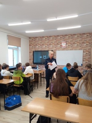 uczniowie siedzą w ławkach policjantka prowadzi prelekcje