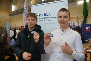 dwóch chłopaków trzyma odblaski w kształcie radiowozu stoją na tle baneru komendy powiatowej policji w Żywcu