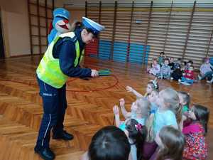 zdjęcie kolorowe zrobione w sali gimnastycznej policjantka rozdaje dzieciom odblaskowe opaski