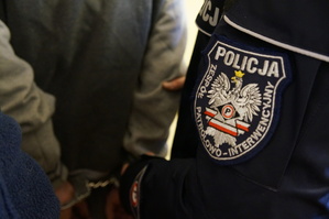 zdjęcie poglądowe kolorowe fragment osoby zatrzymanej z założonymi kajdankami oreaz policjanta