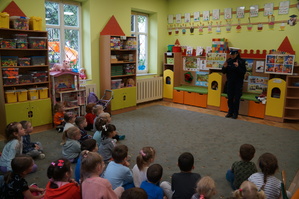 zdjęcie kolorowe zrobione w sali policjantka stoi przed dziećmi i prowadzi prelekcję