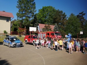 na boisku zaparkowany wóz strażacki i radiowóz obok dzieci strażacy i sznupek