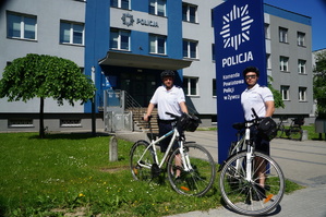 policjanci stoją przed pylonem żywieckiej komendy trzymają rowery w tle budynek komendy