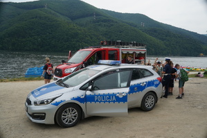 radiowóz policyjny i wóz strażacki nad jeziorem obok stoją dzieci