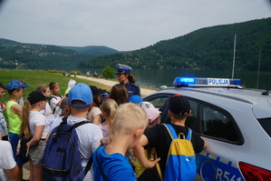 policjantka stoi obok radiowozu obok dzieci w tle jezioro
