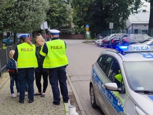 zdjęcie kolorowe fragment radiowozu obok policjanci dają odblaski uczennicom