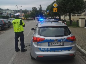 zdjęcie kolorowe przed szkołą stoi zaparkowany radiowóz obok stoi policjant w tle ulica