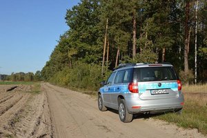 zdjęcie poglądowe samochód policyjny zaparkowany na leśnej drodze obok pole i las