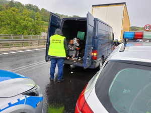 fragment radiowozów w tle otwarty bus w środku którego siedzą osoby obok stoi funkcjonariusz straży granicznej