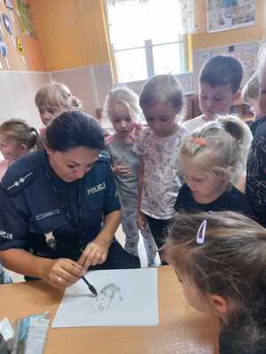 policjantka pokazuje dzieciom w jaki sposób zabezpiecza się ślady