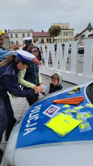 policjantka wręcza odblaski dziecku obok fragment radiowozu