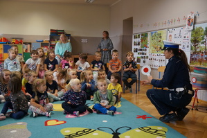 zdjęcie policjantki z boku która kuca w ręce trzyma tarcze do zatrzymywania pojazdów dzieci siedzą przed nią