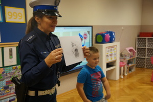 policjantka trzyma zabezpieczone na kartce odciski linii papilarnych chłopczyk stoi obok