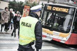 zdjęcie poglądowe policjant stoi przy przejściu dla pieszych w tle ludzie i autobus