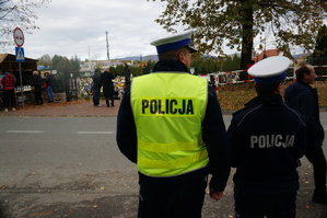 policjanci stoją tyłem w tle cmentarz