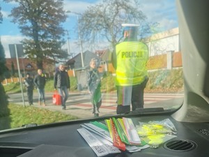 zdjęcie zrobione z wnętrza radiowozu w tle stoi policjant i ludzie na pierwszym planie odblaski