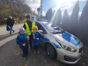 policjantka z dwójką dzieci stoi przy radiowozie dzieci trzymają odblaski