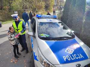 policjantka przy radiowozie stoi z dziewczynką i daje jej odblask