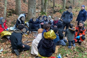 zdjęcie kolorowe osoby siedzą na polanie w lesie obok policjant oraz ratownik medyczny w czasie badania jednej z osób