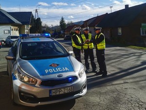 zdjęcie kolorowe radiowóz obok niego stoją trzej policjanci w tle budynki