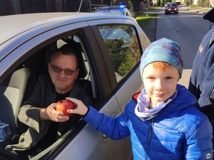 dziecko wręcza kierowcy jabłuszko w tle radiowóz