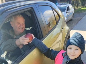 dziecko wręcza innemu kierowcy jabłuszko w tle ulica i radiowóz