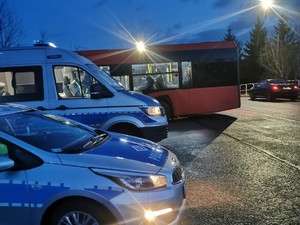 zdjęcie zrobione o świcie kolorowe na pierwszym planie zaparkowane dwa radiowozy w tle autobus i ulica